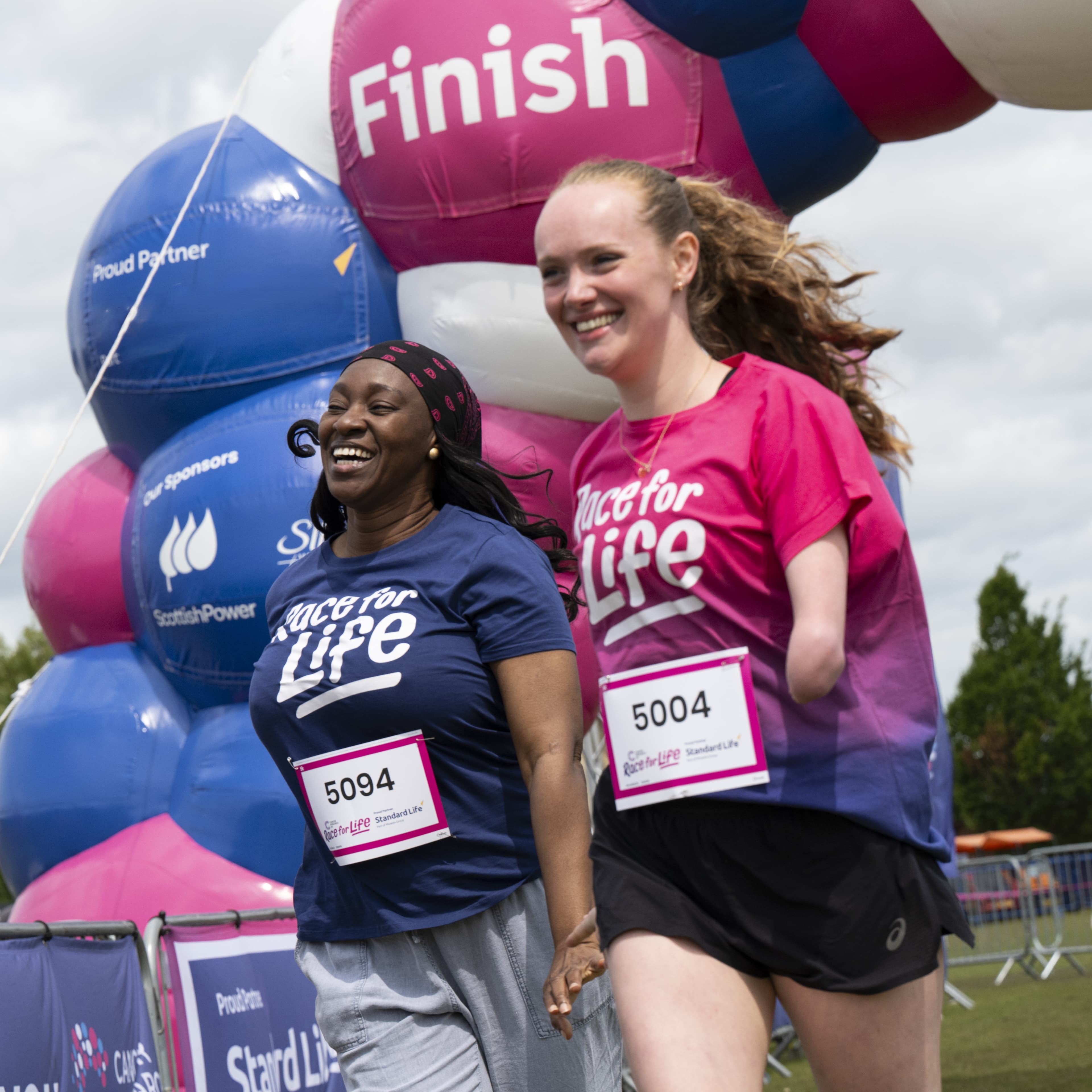 Two young women crossing the finish line holding hands and smiling.