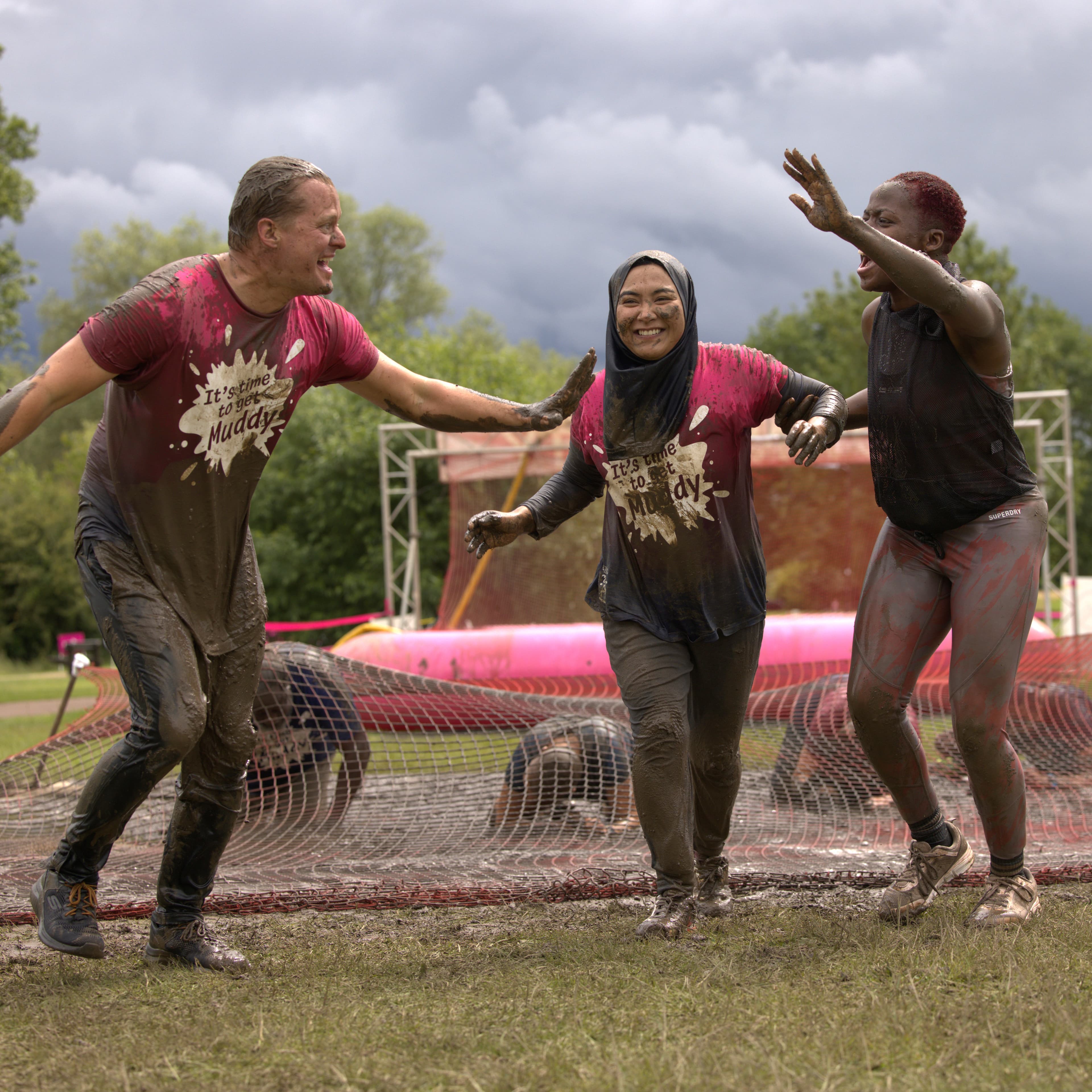 Three participants taking on a Pretty Muddy obstacle with smiles on their faces.