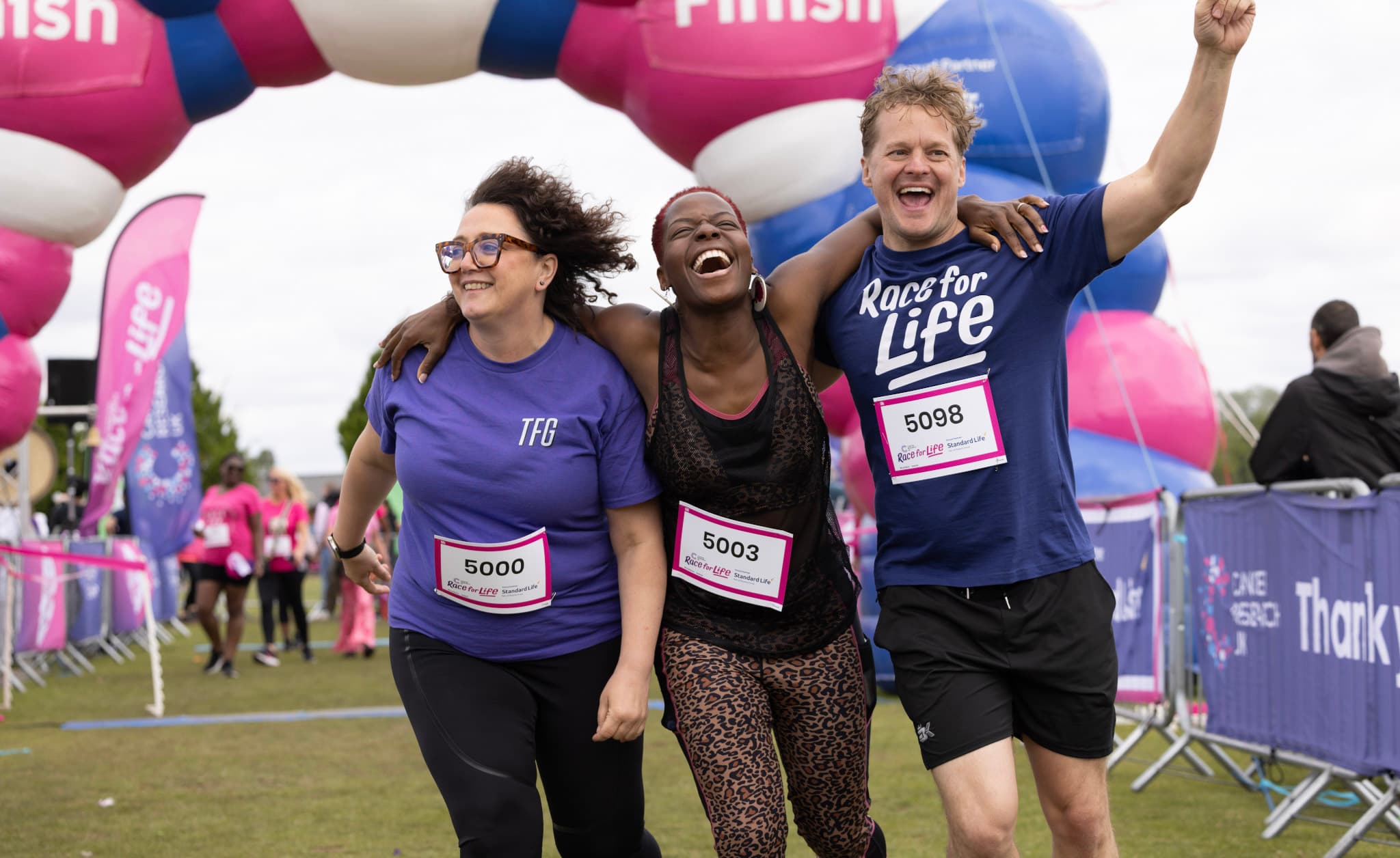 Three Race for Life participants running through the finish line together and laughing.